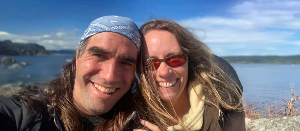 Smiling couple with long hair and bandanna posing outdoors by the ocean.
